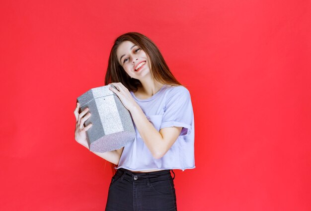 Menina segurando uma caixa de presente de prata e se sentindo feliz.