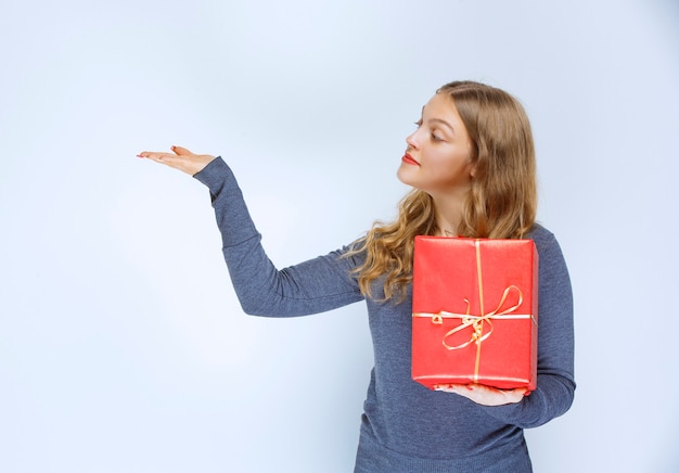 Foto grátis menina segurando uma caixa de presente vermelha e apontando para alguém à esquerda.