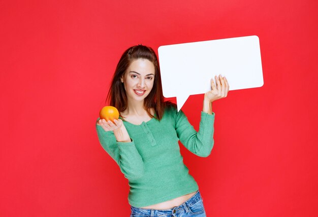 Menina segurando uma laranja fresca e uma placa de informações de retângulo.
