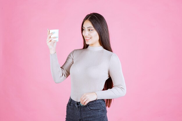 Menina segurando uma xícara de café descartável branca, promovendo-a ou sentindo o cheiro de café fresco