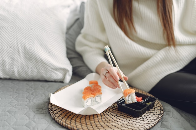 Menina sentada em casa em um sofá com um sushi