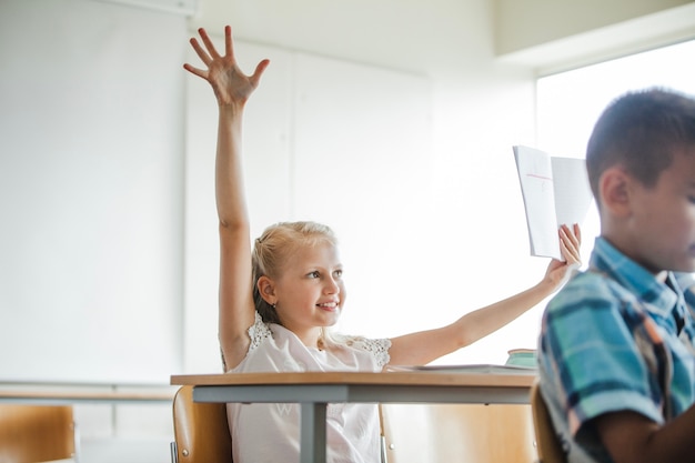 Foto grátis menina sentada na mesa da escola levantando mão