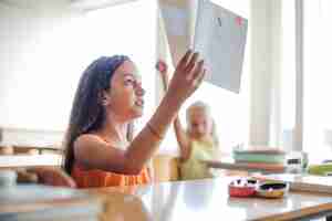 Foto grátis menina sentada na mesa da escola, segurando o caderno