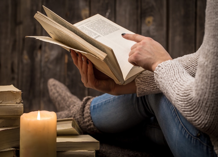Foto grátis menina sentada no chão cercada por muitos livros brancos e uma grande vela