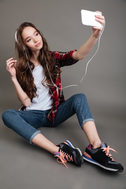 Menina sentada no chão e tomando selfie com fones de ouvido