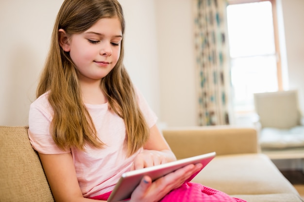 Menina sentada no sofá usa a tabuleta digital na sala de estar