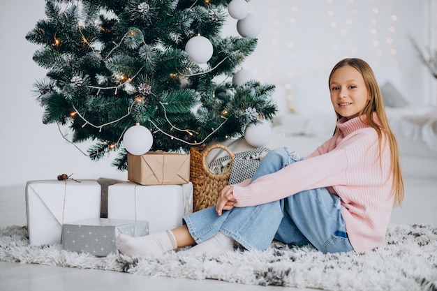Menina sentada perto da árvore de natal