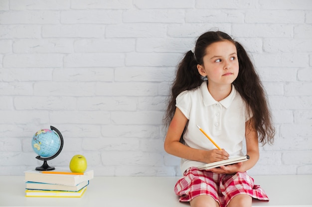 Foto grátis menina sentada segurando lápis de caderno olhando para longe