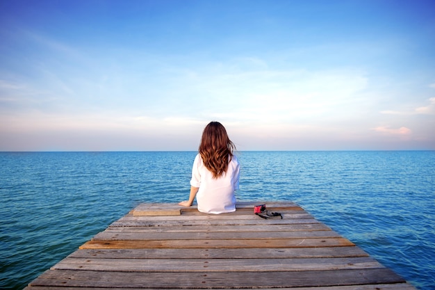 Menina sentada sozinha em uma ponte de madeira no mar. (depressão frustrada)