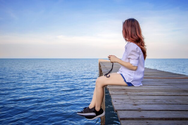 Menina sentada sozinha em uma ponte de madeira no mar. Estilo de tom vintage.