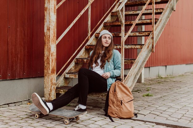 Menina skatista na cidade sentada na escada, visão de longo prazo