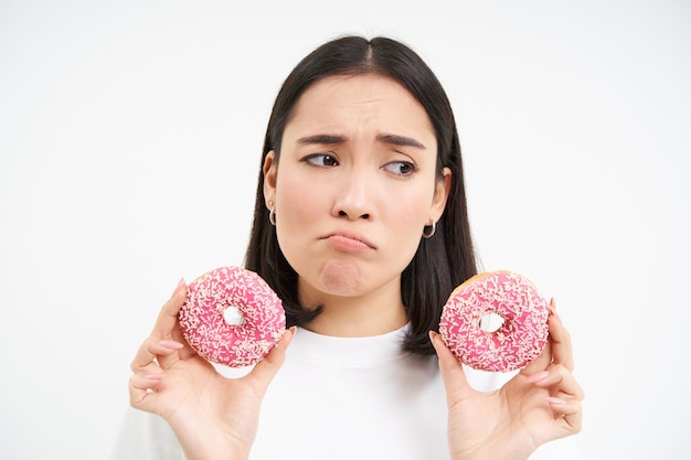 Menina soluçando chateada não pode comer junk food mostra deliciosos donuts vitrificados querem morder o fundo branco