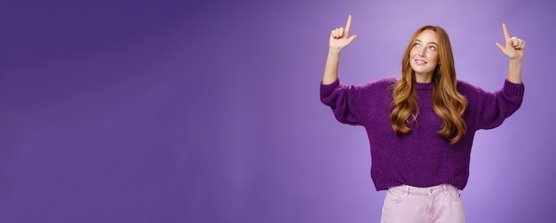 Foto grátis menina sonhadora com cabelo ruivo e sardas em suéter roxo quente e aconchegante levantando as mãos olhando e apontando