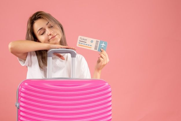 Menina sonolenta com uma mala rosa segurando o ingresso