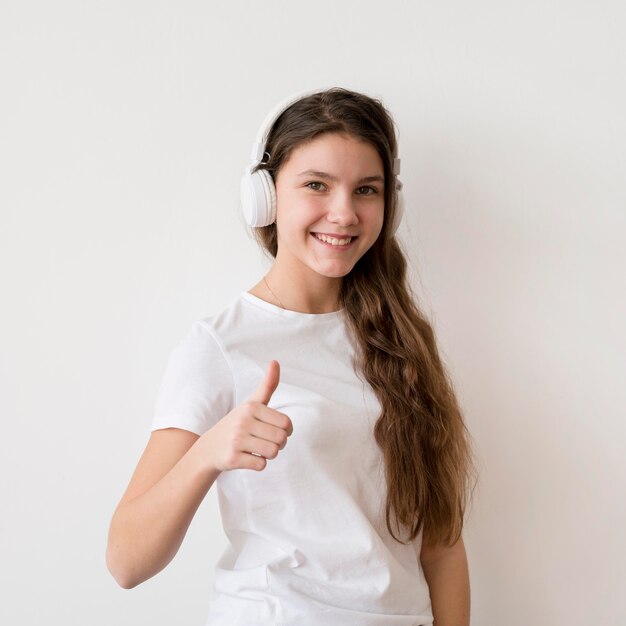 Menina sorridente com fones de ouvido, mostrando sinal de ok