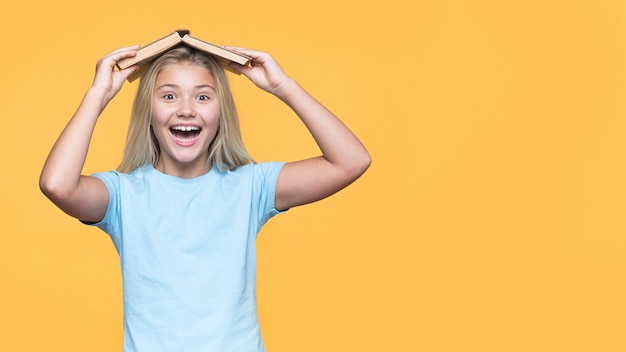 Menina sorridente com livro na cabeça