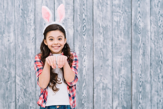 Menina sorridente, com, orelhas bunny, posar, semelhante, coelho, contra, cinzento, escrivaninha madeira