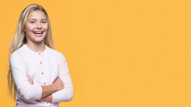 Menina sorridente com os braços cruzados em fundo amarelo