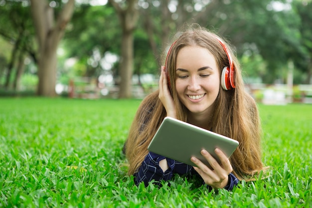 Menina sorridente com tabuleta e fones de ouvido na grama