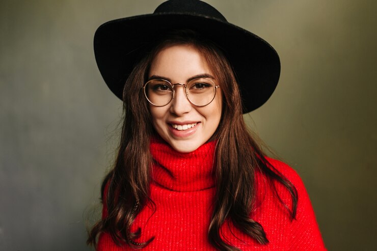 Foto grátis menina sorridente de ótimo humor. foto do modelo com olhos castanhos em uma camisola de malha brilhante e um chapéu na parede cinza.