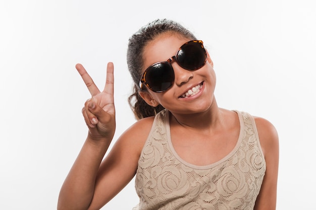 Menina sorridente em óculos de sol gesticulando sinal de paz