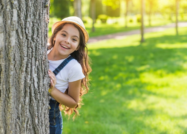 Menina sorridente, escondendo-se atrás de uma árvore
