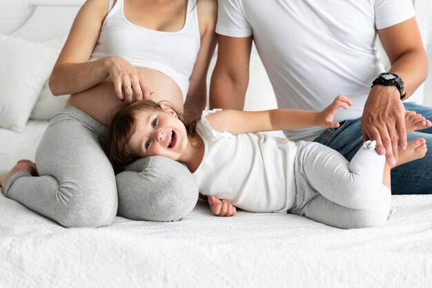 Menina sorridente, ficar na cama com os pais dela