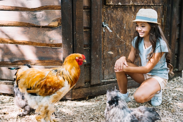 Menina sorridente, olhando para as galinhas na fazenda