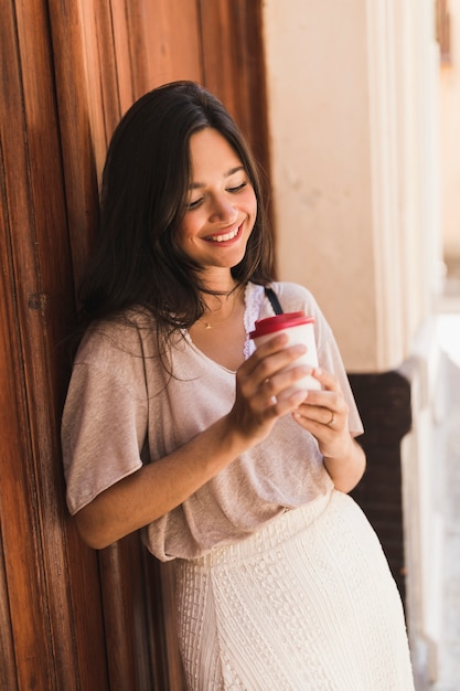 Menina sorridente, olhando para o copo de café descartável