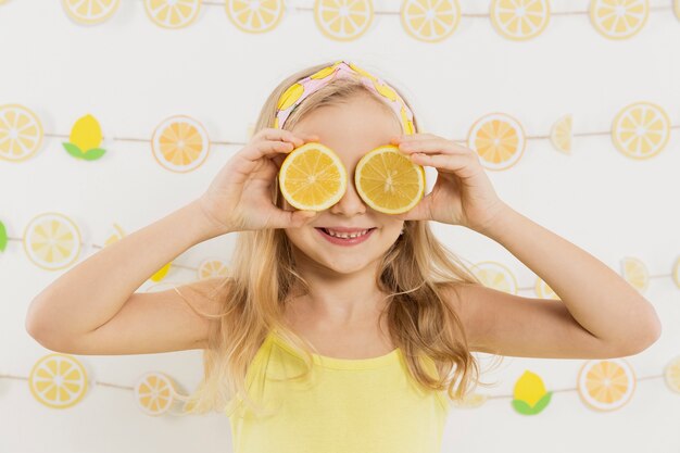 Menina sorridente posando enquanto cobria os olhos com rodelas de limão
