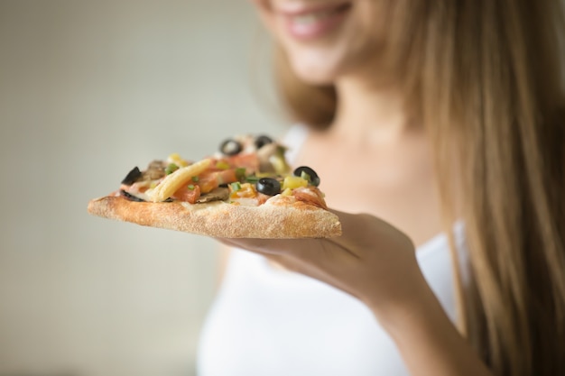 Foto grátis menina sorridente segurando uma fatia de pizza na mão