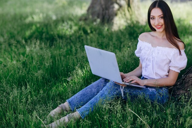 menina sorridente sentado na grama com um portátil
