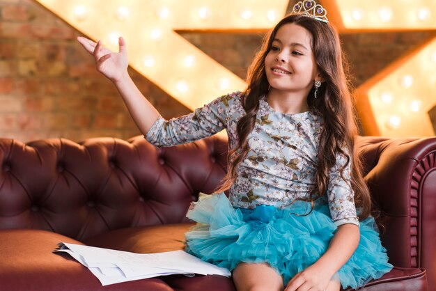 Menina sorridente usando coroa sentado no sofá com roteiros