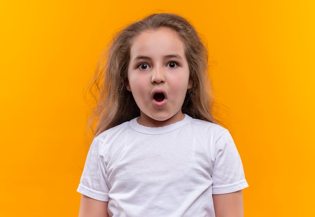Foto grátis menina surpresa da escola vestindo camiseta branca abrindo a boca em fundo laranja isolado