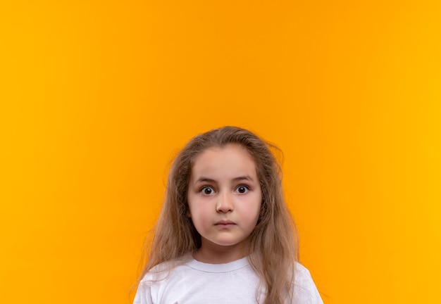 Menina surpresa da escola vestindo camiseta branca em fundo laranja isolado