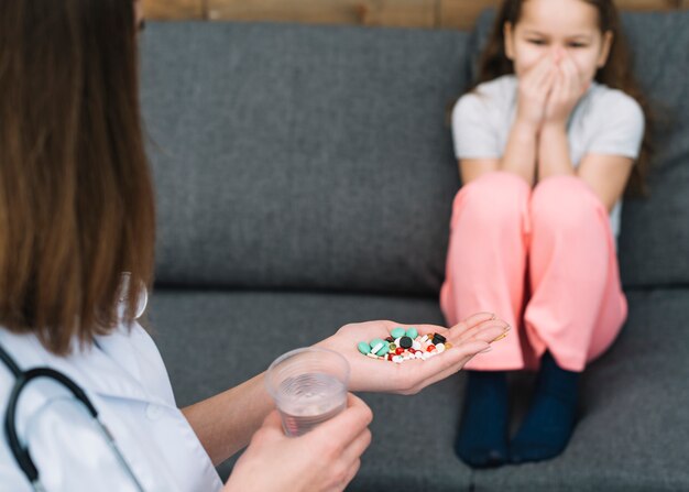 Menina tem medo de seu médico feminino dando remédio e copo de água na mão