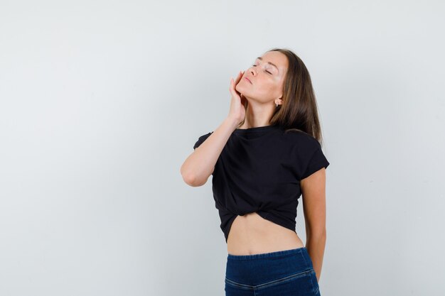 Menina tocando a bochecha com os olhos fechados em uma blusa preta