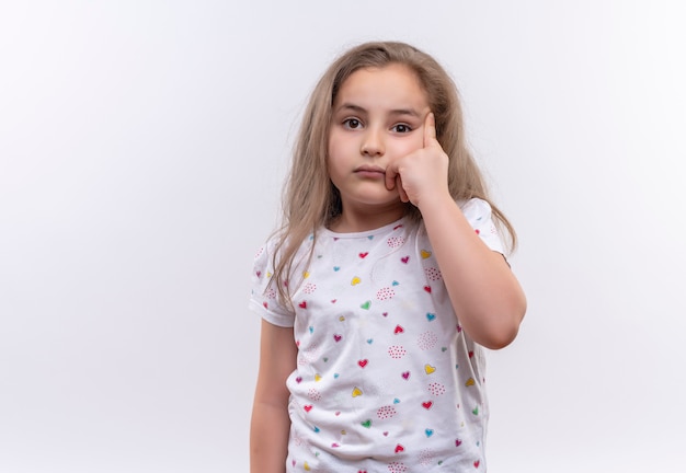 Menina triste da escola vestindo uma camiseta branca colocando o dedo no olho em um fundo branco isolado