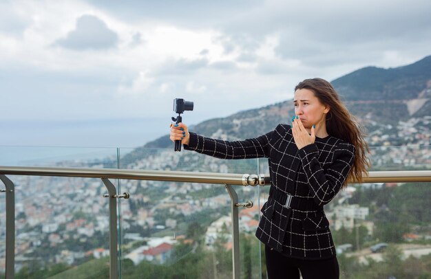 Menina triste do blogueiro está tomando selfie segurando a mão na boca no contexto da vista da cidade