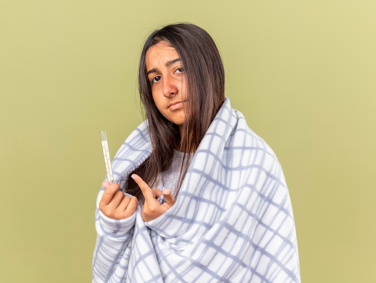 Foto grátis menina triste e doente embrulhada em xadrez segurando e aponta para um termômetro isolado em verde oliva