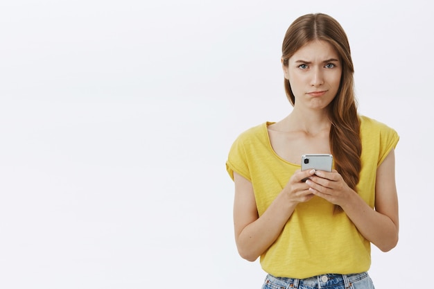 Foto grátis menina triste indecisa e sombria parecendo chateada, segurando um smartphone