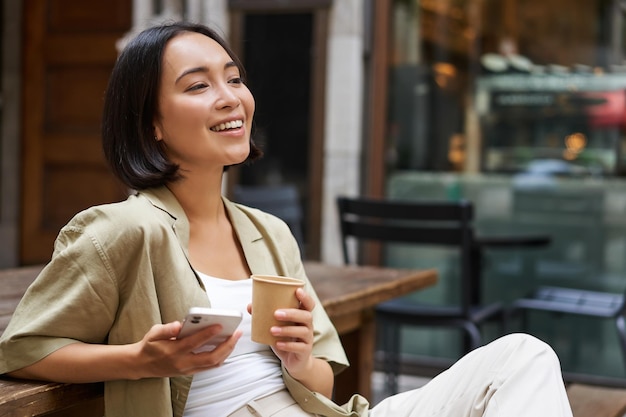 Menina urbana elegante senta-se com seu telefone no café bebe café e conversa navegando nas mídias sociais em s