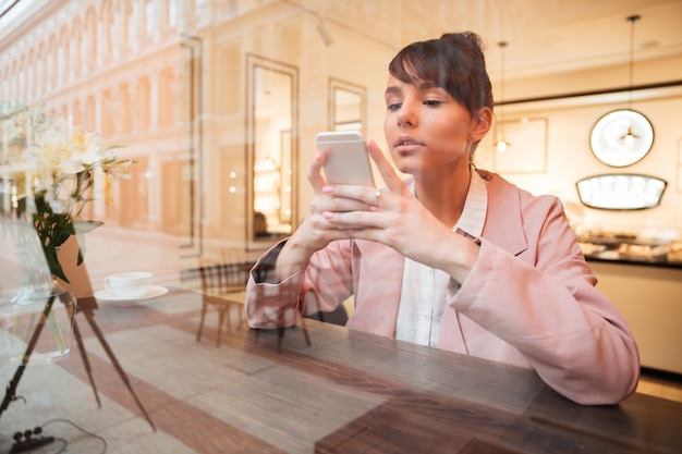 Menina usando telefone celular enquanto está sentado na mesa de café