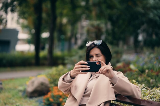 Menina usando um telefone inteligente em um parque da cidade, sentado num banco