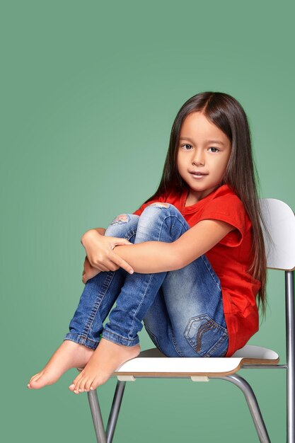 menina vestindo t-curta vermelha e posando na cadeira sobre fundo verde