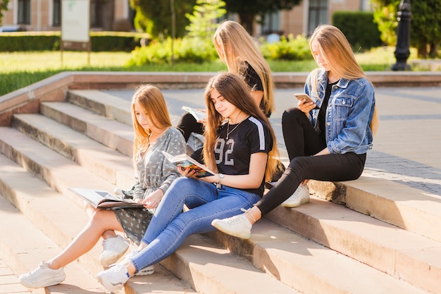 Meninas adolescentes, leitura, livros, e, usando, smartphone, ligado, passos