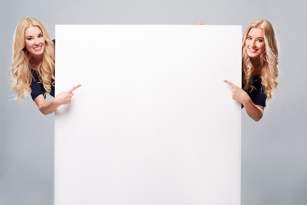 Meninas adultas apontando para um cartaz em branco