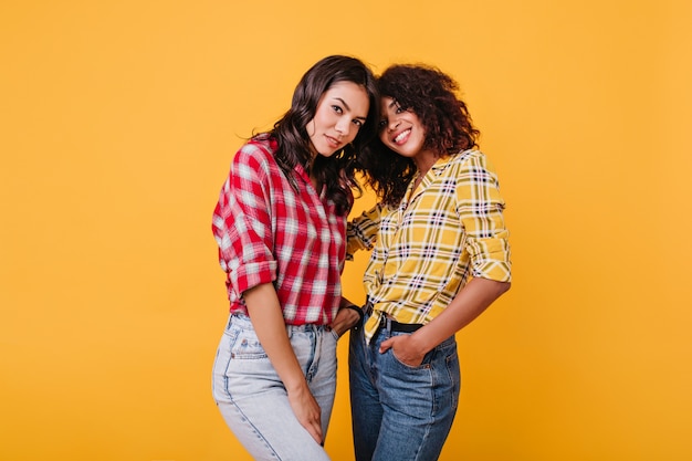 Meninas com cabelo curto escuro olham misteriosamente. Senhoras com camisas coloridas se abraçam.