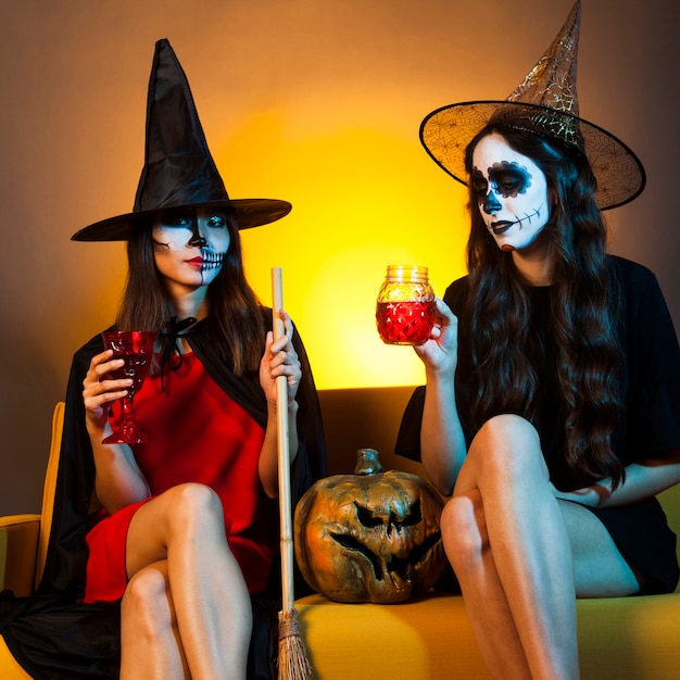 Meninas de Halloween no sofá com abóbora e bebidas