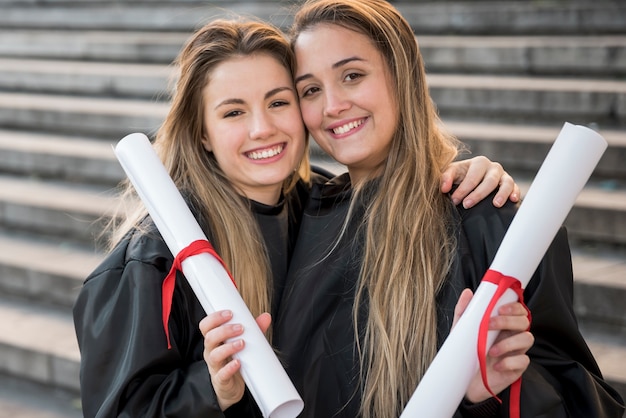 Meninas de vista frontal segurando seus certificados de faculdade